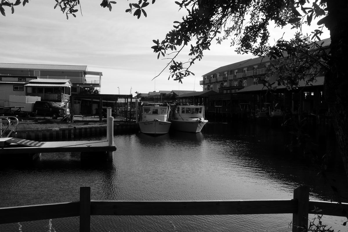 Two boats moored at docks in a canal, with buildings on the far bank