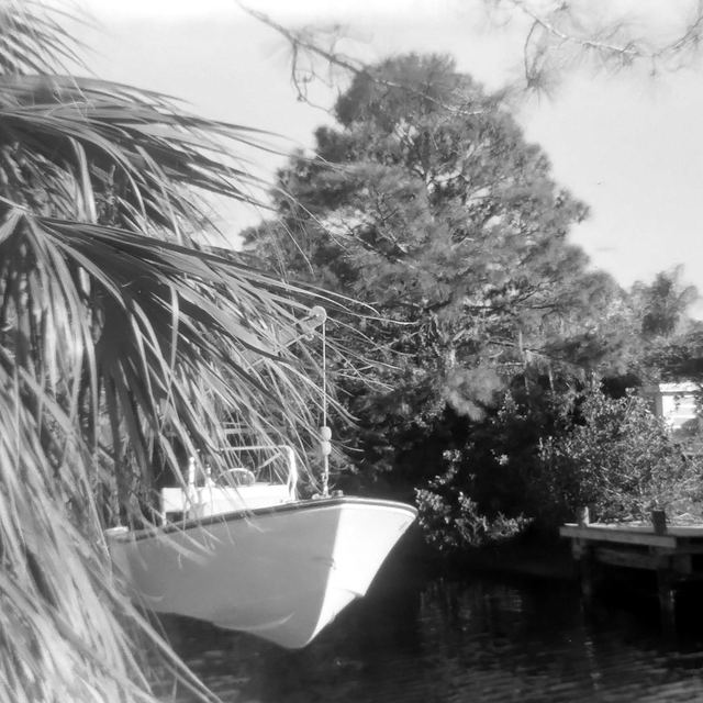 A small boat tied up at a private dock on a palm-lined canal in Englewood, in black and white