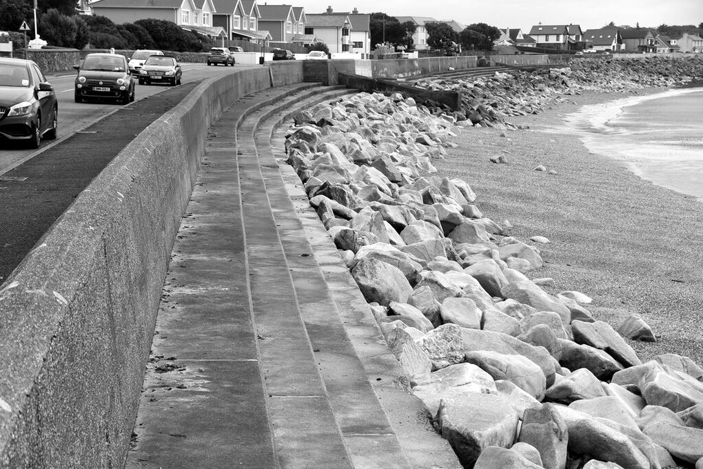 Rock riprap piled along the foot of a concrete seawall beside a beach
